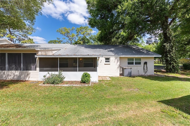 back of house with a yard, a shingled roof, a sunroom, and central AC