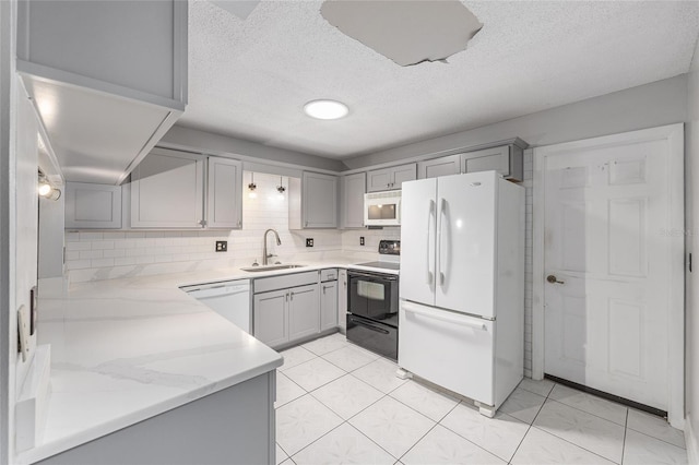 kitchen featuring white appliances, a textured ceiling, tasteful backsplash, a sink, and gray cabinetry