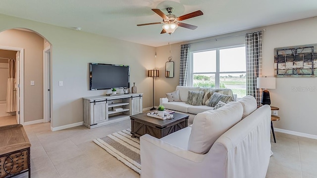 living area featuring light tile patterned floors, arched walkways, ceiling fan, and baseboards
