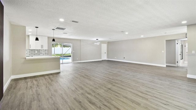 unfurnished living room featuring light wood-style floors, a textured ceiling, recessed lighting, baseboards, and visible vents
