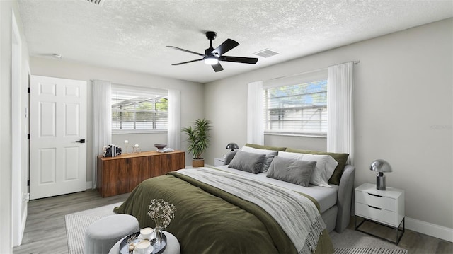 bedroom with ceiling fan, a textured ceiling, visible vents, wood finished floors, and baseboards