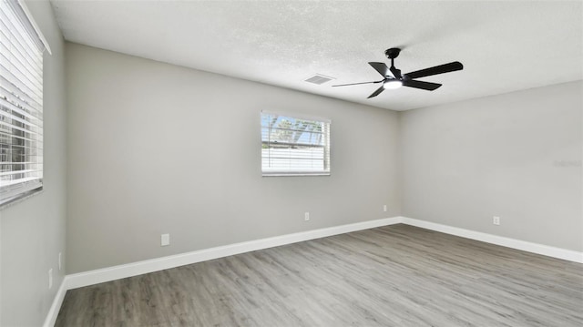 unfurnished room with a ceiling fan, a textured ceiling, visible vents, wood finished floors, and baseboards