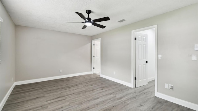 unfurnished bedroom featuring ceiling fan, a textured ceiling, baseboards, wood finished floors, and visible vents
