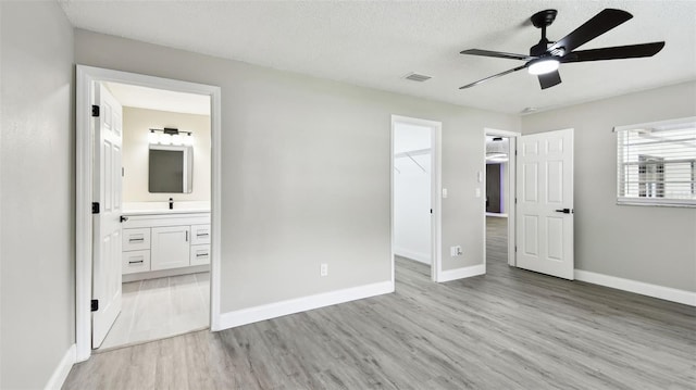 unfurnished bedroom featuring a spacious closet, baseboards, light wood-style flooring, and visible vents