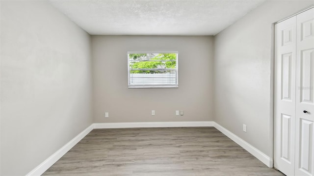 spare room with baseboards, a textured ceiling, and light wood-style flooring