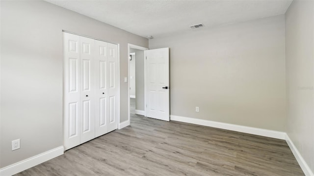 unfurnished bedroom with visible vents, baseboards, wood finished floors, and a closet