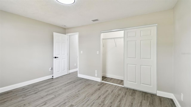 unfurnished bedroom with baseboards, visible vents, wood finished floors, and a closet