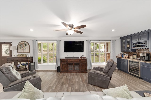 living area with ceiling fan, crown molding, light wood-type flooring, wine cooler, and indoor bar
