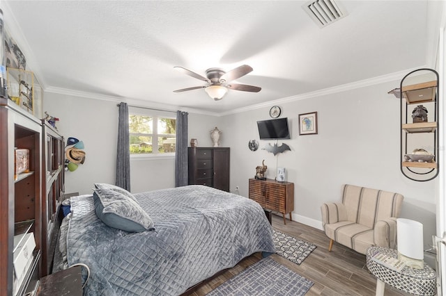 bedroom featuring a ceiling fan, baseboards, wood finished floors, visible vents, and ornamental molding