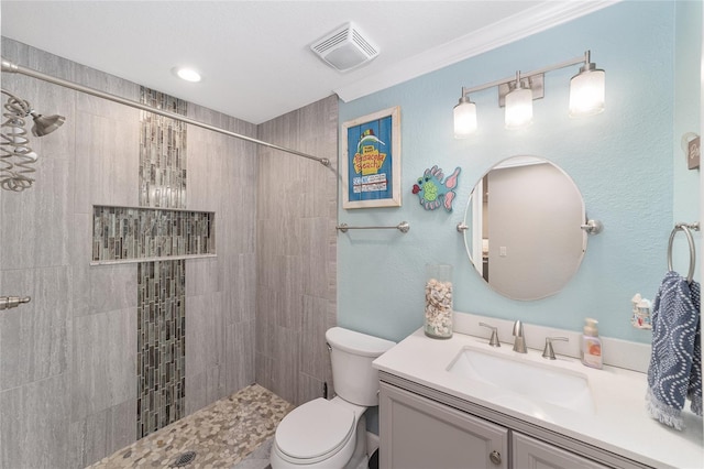 bathroom with toilet, visible vents, tiled shower, and vanity
