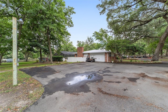 exterior space with fence, brick siding, a garage, aphalt driveway, and a chimney
