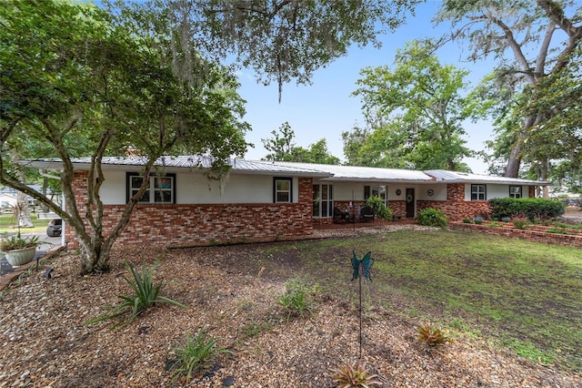 ranch-style home featuring brick siding, stucco siding, and metal roof