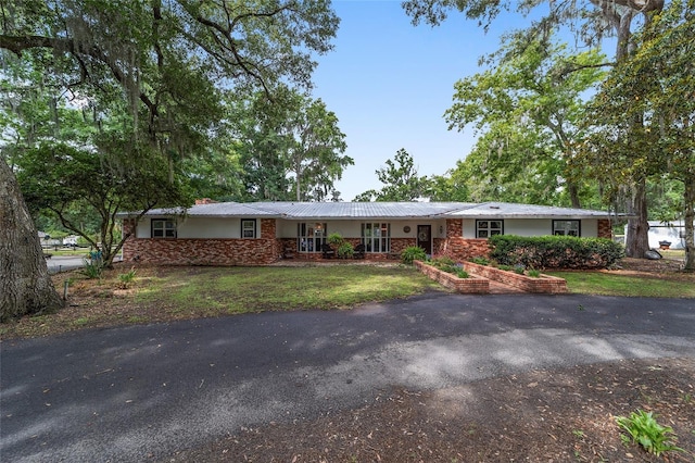 ranch-style house featuring a front lawn, aphalt driveway, stone siding, a chimney, and metal roof