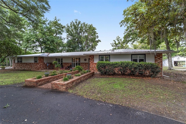 ranch-style home with metal roof, stucco siding, a front lawn, and brick siding