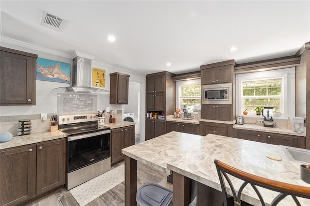 kitchen featuring visible vents, dark brown cabinets, wall chimney range hood, plenty of natural light, and appliances with stainless steel finishes