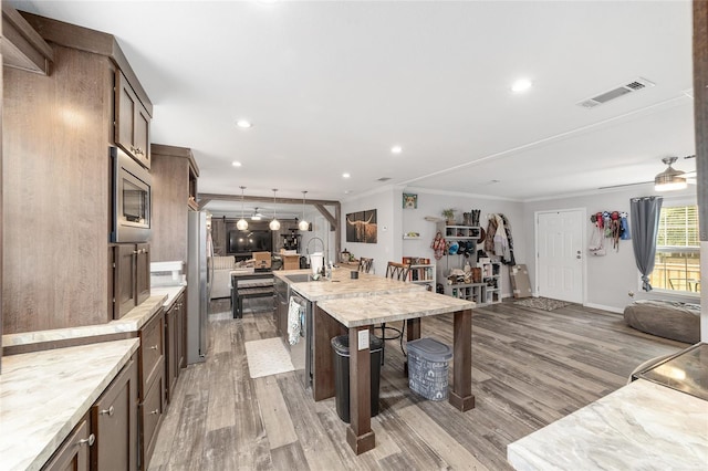 interior space featuring visible vents, a center island with sink, ornamental molding, stainless steel appliances, and light wood-style flooring