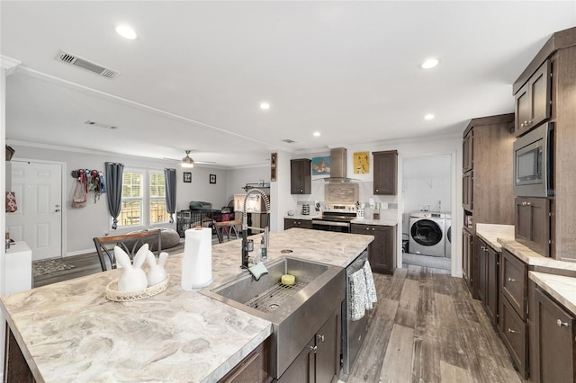 kitchen featuring visible vents, washer and dryer, dark wood-style floors, wall chimney exhaust hood, and stainless steel appliances