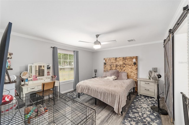 bedroom featuring visible vents, a barn door, wood finished floors, baseboards, and ornamental molding