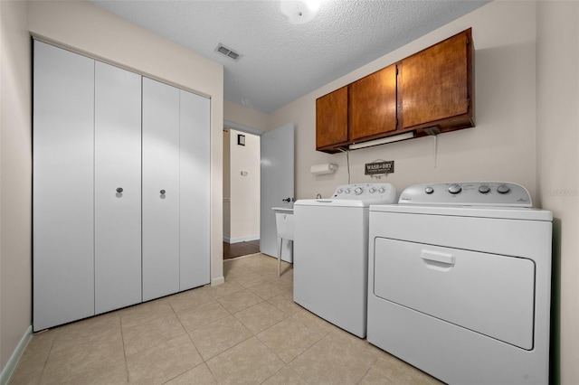 laundry area with cabinet space, independent washer and dryer, a textured ceiling, light tile patterned flooring, and baseboards