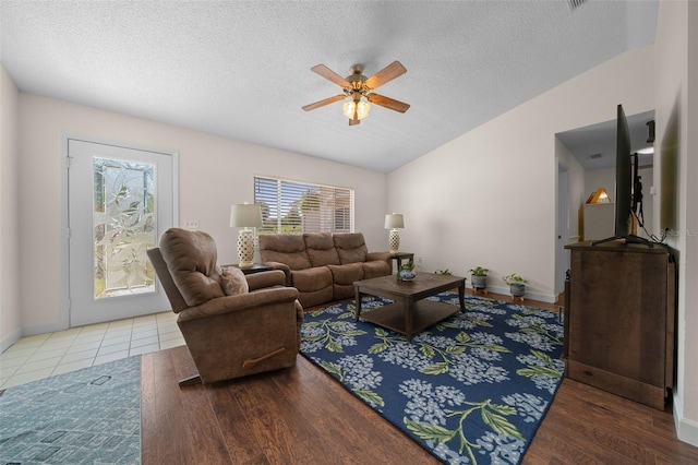living area featuring plenty of natural light, ceiling fan, a textured ceiling, vaulted ceiling, and baseboards
