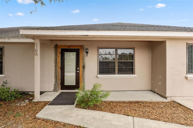 entrance to property with stucco siding and a shingled roof
