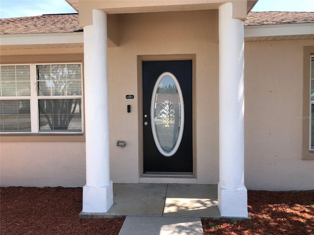 view of exterior entry with a shingled roof and stucco siding