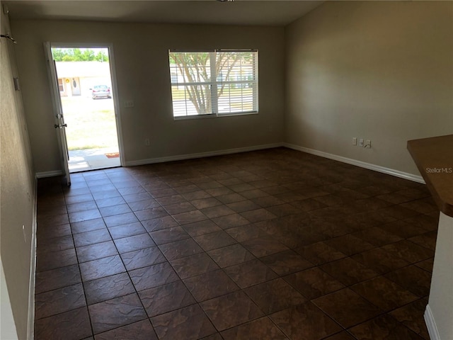 unfurnished room featuring baseboards, dark tile patterned floors, and a healthy amount of sunlight