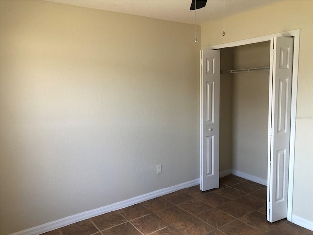 unfurnished bedroom featuring baseboards, ceiling fan, a closet, and dark tile patterned floors