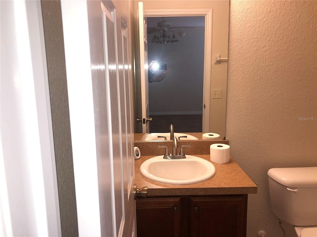 half bath featuring vanity, a textured wall, and toilet