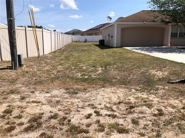 view of yard with an attached garage, fence, and driveway
