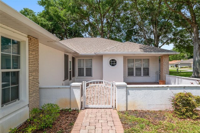 11146 SW 68th Ct, Ocala, FL 34476 - view of exterior entry featuring fence, roof with shingles, stucco siding, brick siding, and a gate