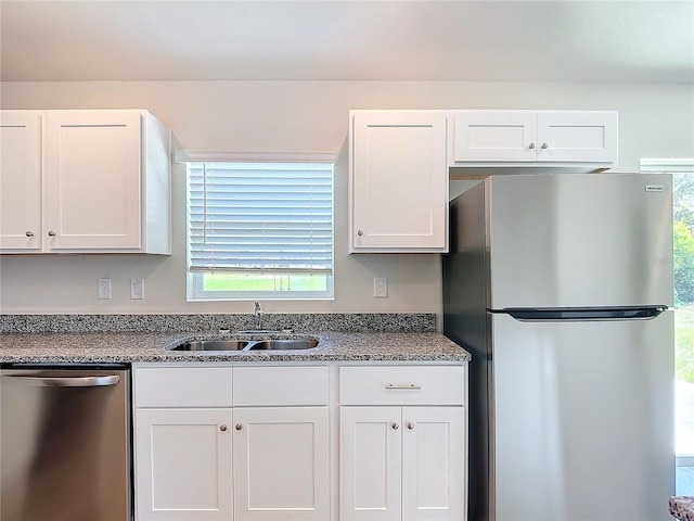kitchen with white cabinets, stone countertops, appliances with stainless steel finishes, and a sink
