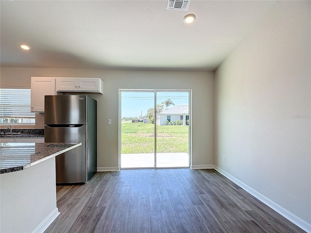 kitchen featuring freestanding refrigerator, visible vents, dark wood-style floors, and dark stone counters