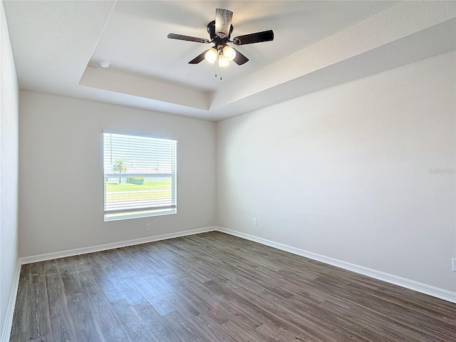 empty room with dark wood-style flooring, baseboards, and a raised ceiling