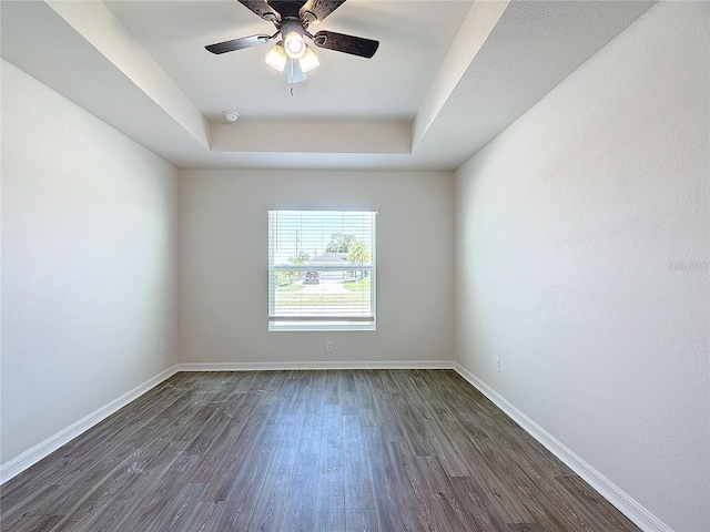 unfurnished room with a raised ceiling, baseboards, a ceiling fan, and dark wood finished floors