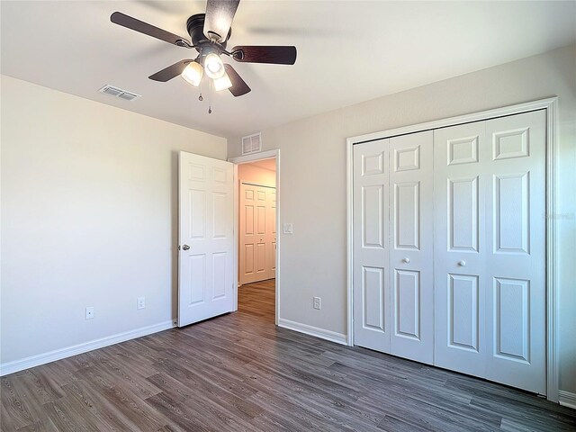 unfurnished bedroom with dark wood-style flooring, baseboards, visible vents, and a closet