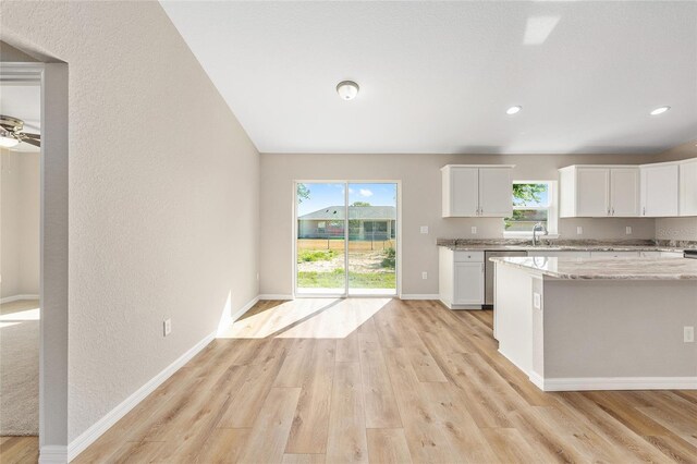 kitchen with light stone countertops, a sink, light wood-style floors, white cabinetry, and baseboards