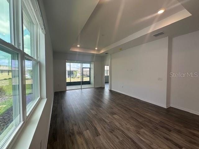 spare room with a raised ceiling, dark wood finished floors, recessed lighting, baseboards, and visible vents