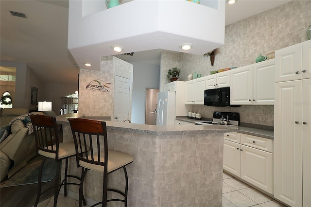 kitchen with black microwave, a kitchen breakfast bar, range with electric cooktop, freestanding refrigerator, and visible vents