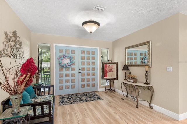 entryway with visible vents, a textured ceiling, baseboards, and wood finished floors