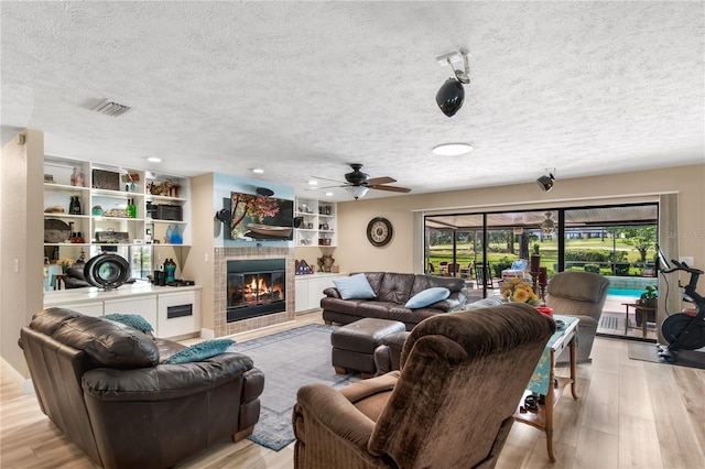 living room with a textured ceiling, a tiled fireplace, ceiling fan, and light wood-type flooring