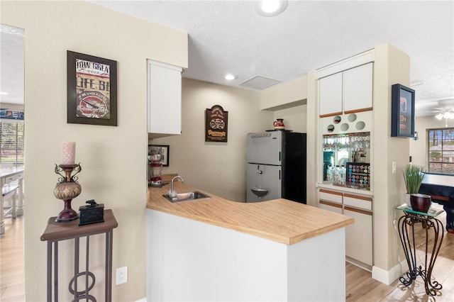 kitchen featuring a sink, freestanding refrigerator, a peninsula, and a textured ceiling
