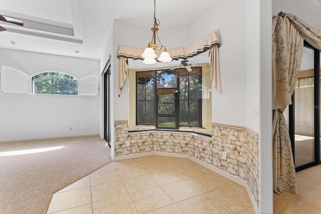 unfurnished dining area featuring wainscoting, an inviting chandelier, light carpet, and light tile patterned floors