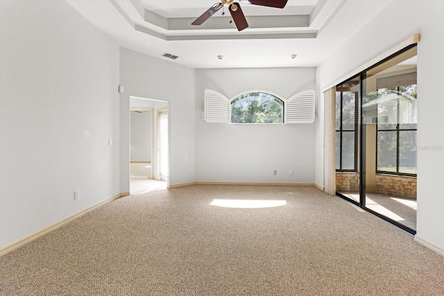 empty room featuring visible vents, carpet, ceiling fan, and a tray ceiling