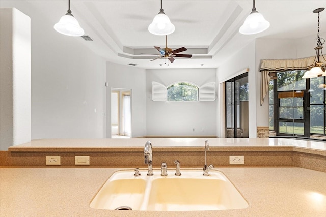 kitchen with visible vents, ceiling fan, a tray ceiling, a sink, and hanging light fixtures