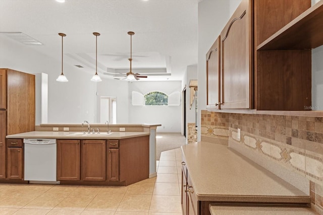 kitchen with white dishwasher, a sink, a tray ceiling, and light countertops