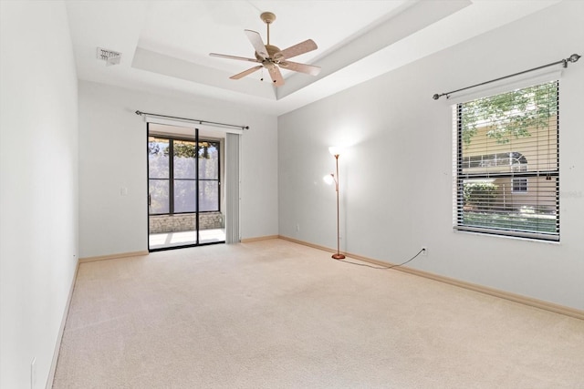 spare room featuring carpet floors, visible vents, baseboards, a raised ceiling, and a ceiling fan