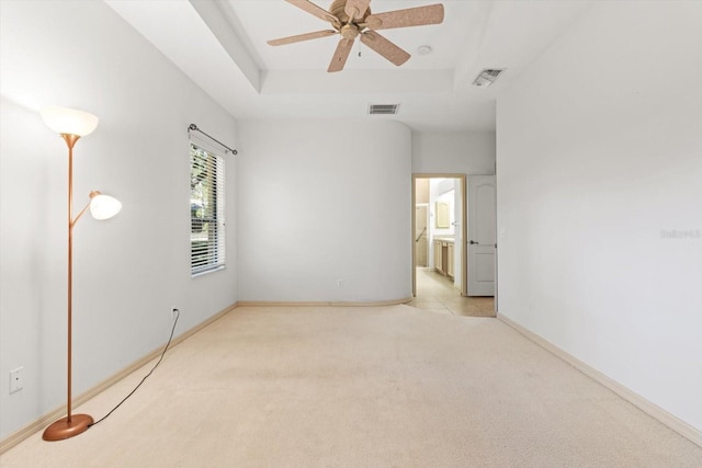 carpeted empty room featuring baseboards, a tray ceiling, visible vents, and ceiling fan