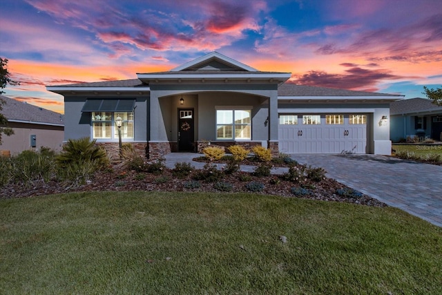 view of front of house with stone siding, decorative driveway, stucco siding, an attached garage, and a yard