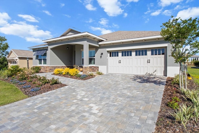 view of front facade featuring decorative driveway, an attached garage, stone siding, and stucco siding